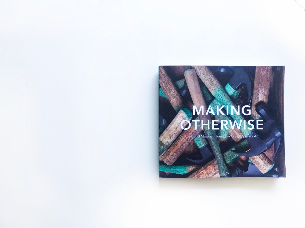 The front cover of the catalogue "Making Otherwise Craft and Material Fluency in Contemporary Art" shows white text superimposed overtop of an image of an artwork by Marc Courtmanche. The artwork image is a closeup of hammers with teal and wooden handles piled up together. 